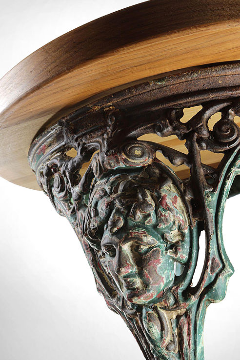 a traditional bistro table consisting of a cast iron base with scrolls and masques finished with a solid timber top