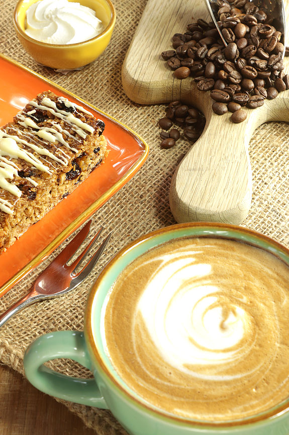 a cup of white Americano coffee, beside luxury flapjack, a finger bowl of whipped cream and a scoop of fresh coffee beans