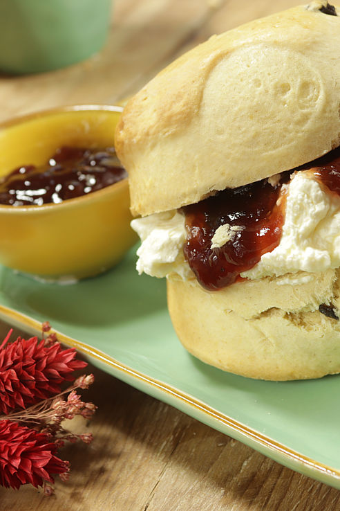 close-up of a strawberry jamd and clotted cream scone on a mint green platter