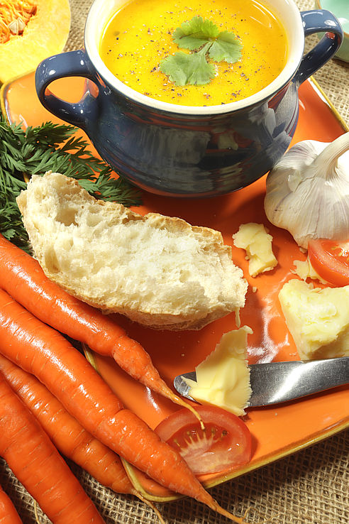 a blue bowl of parsnip soup with cheese and tomato piece son an orange platter
