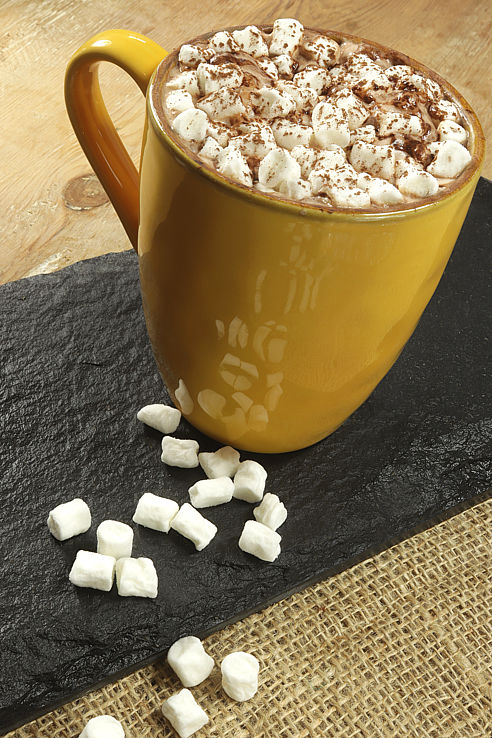 a ochre yellow mug filled with hot chocolate and topped with minni marsh-mallows on a slate
