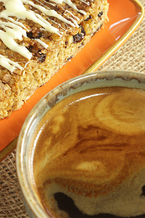 a slice of luxury fruit flapjack on an orange platter beside a cup of americano coffee