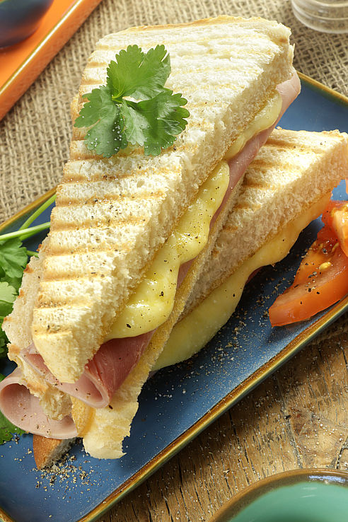 a tasty griddled bread sandwich filled with rolled ham pieces and melted cheese, pepper and salt on a blue platter with salad