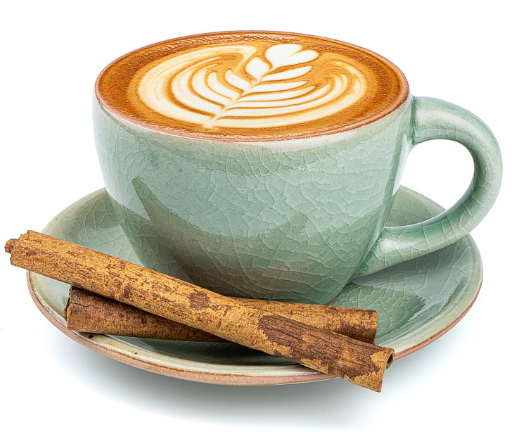 a crackle-glazed green coffee cup and saucer with a decorative leaf design on the coffee and cinnamon sticks in the saucer