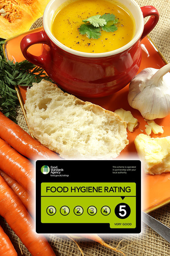 A red bowl of carrot and coriander soup on an orange platter together with garlic, frsh bread, chees and carrots