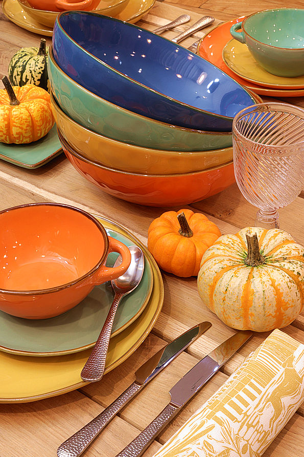 Colourful tableware with designer cutlery, fine art napkins and glorious pumpkins set on a fine solid wood table
