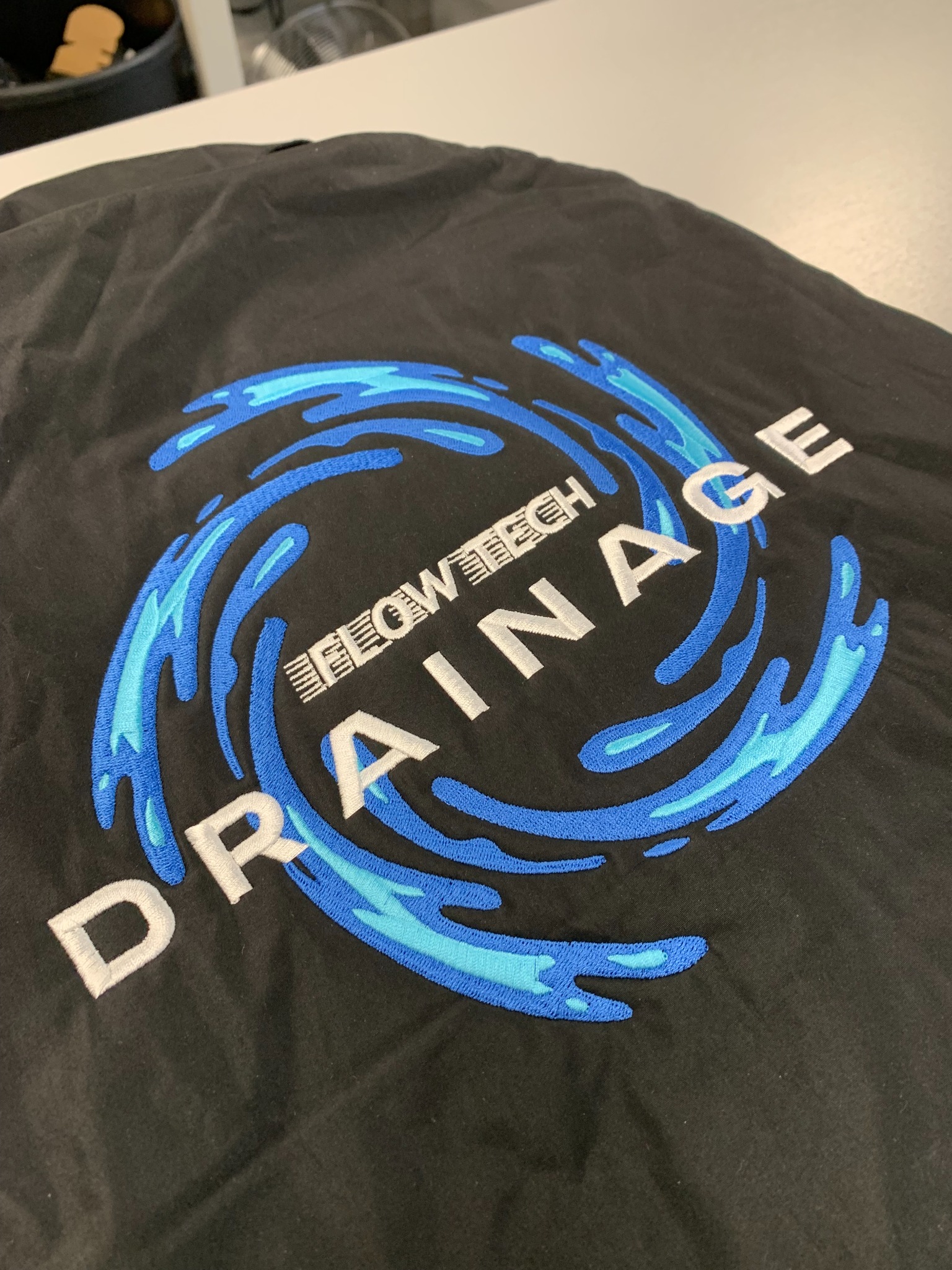 Flowtech Drainage logo Embroidery on grey workwear, produced by The Thread Studio