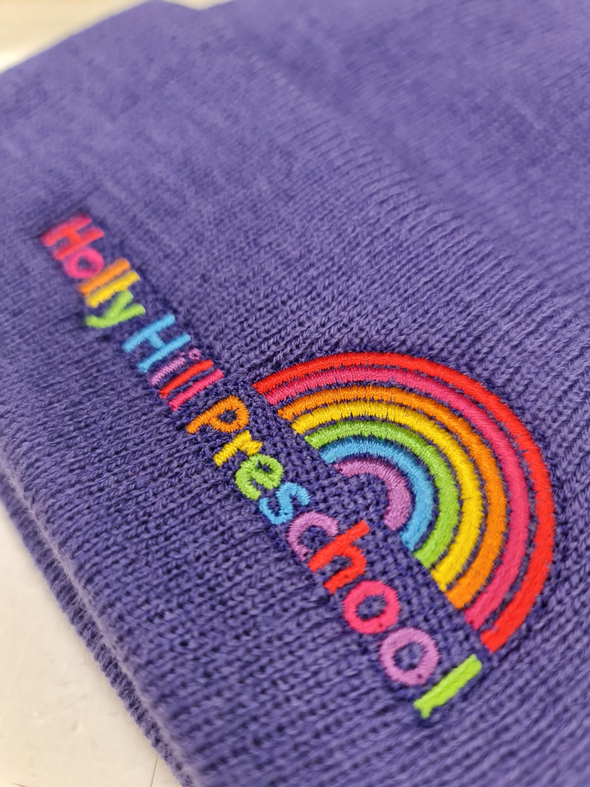 Close-up of colourful Holly Hill Pre-School lettering and rainbow embroidered on purple fabric