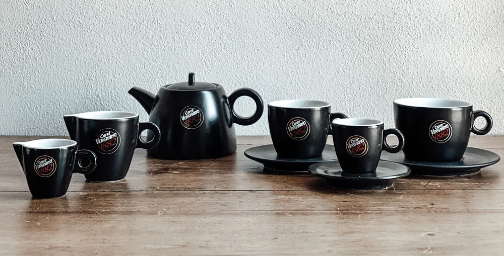 Branded Caffè Vergnano cups, saucers and a teapot on a wooden table