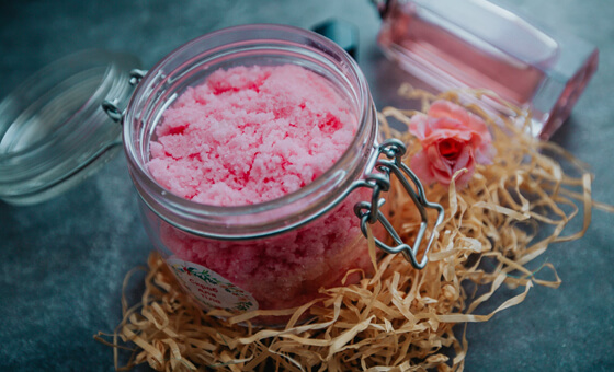 a glass jar filled with bright pink body scrub